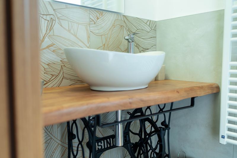 Bagno di Curt de Gat: lavabo sul piano in legno, base di macchina da cucire Singer e carta da parati a foglie