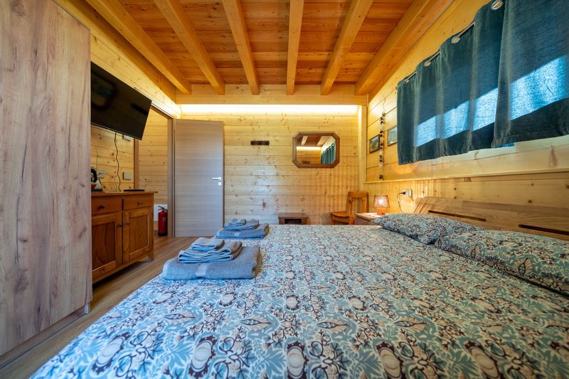 Camera Tirlo vista dal letto: specchio, credenza e porta, soffitto a travi a vista