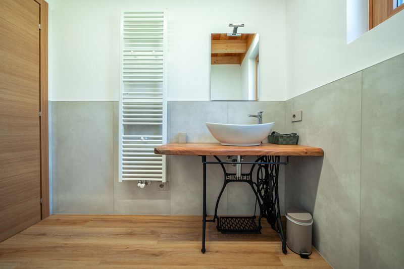 Bagno di Tirlo: lavabo sul piano in legno appoggiato alla base di una macchina da cucire Singer, scaldasalviette
