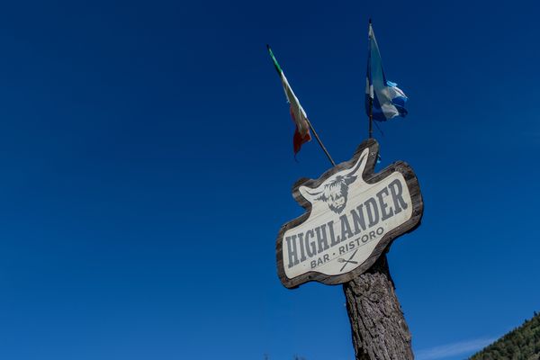 L’insegna Highlander su un palo di legno, con le bandiere e il cielo blu