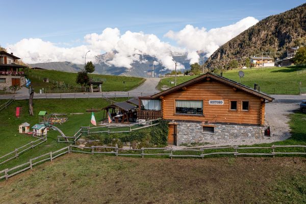 Il ristoro visto da un drone a bassa quota, con il prato, i recinti e le nuvole sulle montagne